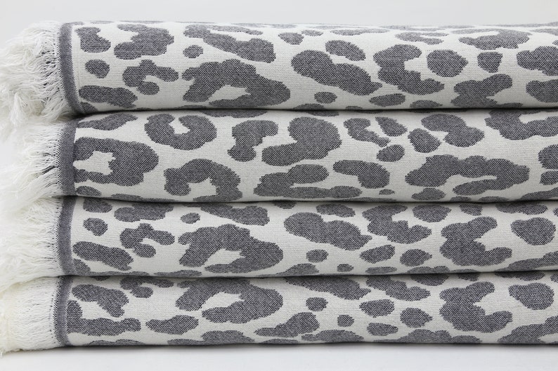 May include: A stack of four gray and white towels with a leopard print pattern. The towels have white fringe around the edges.