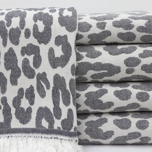 May include: A stack of gray and white towels with a leopard print pattern. The towels have a fringe on the bottom.