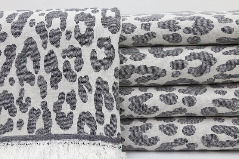 May include: A stack of gray and white towels with a leopard print pattern. The towels have a fringe on the bottom.