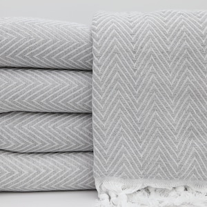 May include: A stack of four grey and white chevron patterned towels with white fringe.