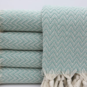 May include: A stack of five teal blue and white patterned towels with fringe. The towels are folded and stacked on a white surface.