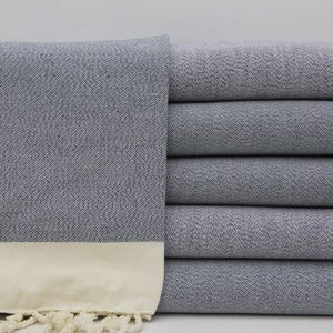 May include: A stack of gray Turkish towels with a white fringe. The towels are made of cotton and have a soft, absorbent texture.