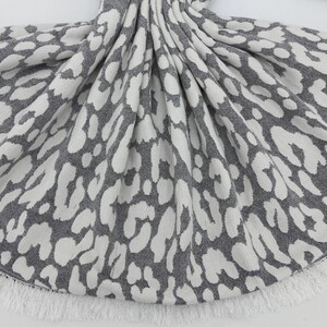 May include: Gray and white knitted throw blanket with a leopard print pattern and a white fringe border.