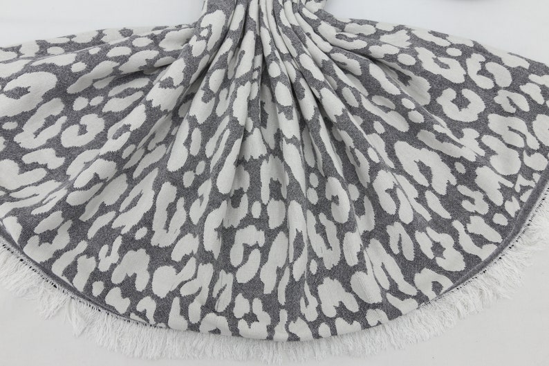 May include: Gray and white knitted throw blanket with a leopard print pattern and a white fringe border.