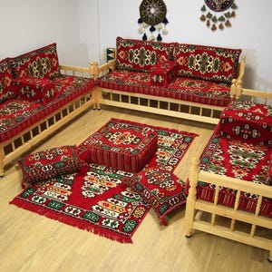 May include: A traditional Middle Eastern seating set with a wooden frame and red, green, and white patterned cushions. The set includes a sofa, two chairs, and several throw pillows. The set is arranged on a red and green patterned rug.
