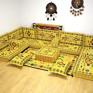 May include: A yellow and black patterned floor seating set with multiple cushions and a small square ottoman. The set is arranged in a U-shape and is perfect for a living room or family room.