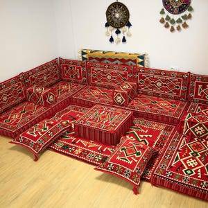 May include: A red and gold patterned floor seating set with multiple cushions and a small square ottoman. The set is arranged in a U-shape and features intricate geometric designs.