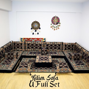 May include: A black and gold patterned U-shaped sofa set with a matching ottoman. The sofa is made of fabric and has a traditional design. The set is arranged in a living room with two dreamcatchers hanging on the wall.