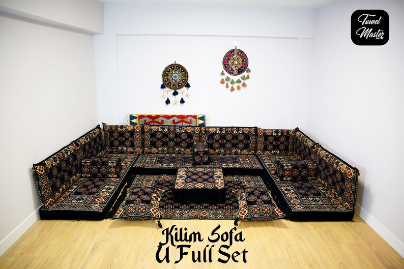May include: A black and gold patterned U-shaped sofa set with a matching ottoman. The sofa is made of fabric and has a traditional design. The set is arranged in a living room with two dreamcatchers hanging on the wall.