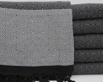 May include: A black and white patterned Turkish towel with fringe. The towel is folded and stacked with other towels in the same pattern.