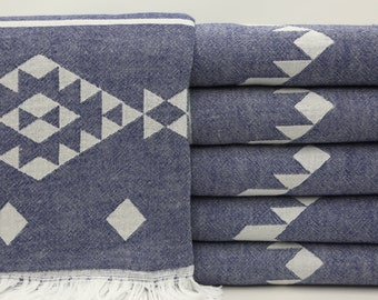 May include: A stack of six blue and white patterned Turkish towels with fringe. The towels feature a geometric design with white diamonds and triangles on a dark blue background.