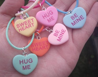 Op de afbeelding: Een set van zes kleurrijke hartvormige kettingen met verschillende boodschappen, waaronder "Sweet Heart", "Hug Me" en "Be Mine".