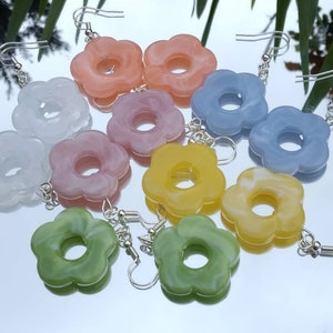 Puede incluir: Un conjunto de 8 pendientes de colores con forma de flor. Los pendientes están hechos de un material plástico marmoleado y tienen un cierre de gancho plateado. Los colores incluyen azul claro, rosa claro, amarillo claro, verde claro y blanco.