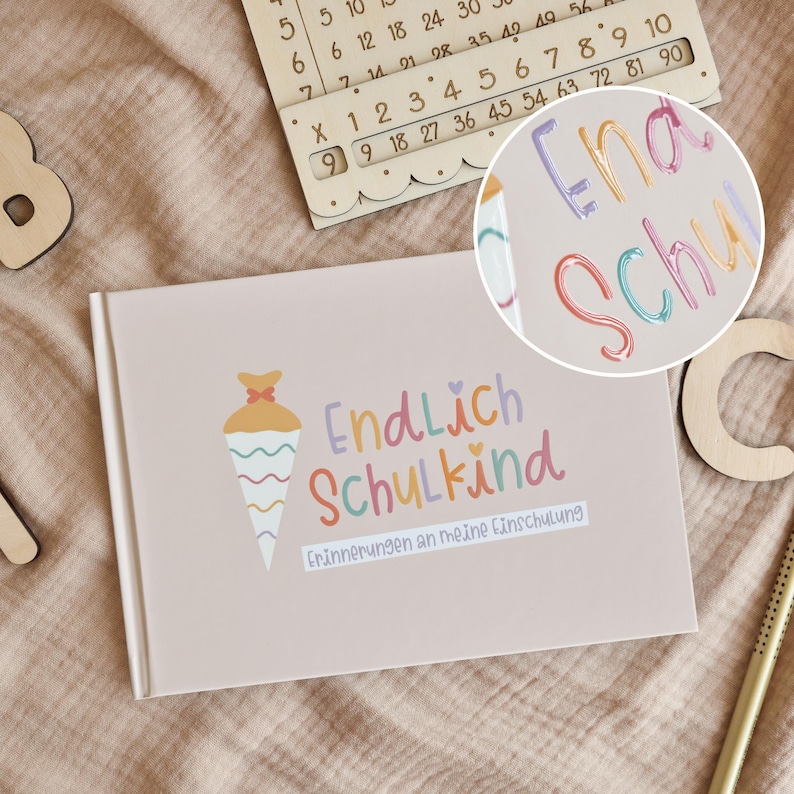 Peut inclure: Un livre rectangulaire rose clair avec un graphique de c&ocirc;ne color&eacute; et le texte Endlich Schulkind Erinnerungen an meine Einschulung. La couverture pr&eacute;sente des lettres pastel en violet, orange et rose, avec une petite ic&ocirc;ne de c&oelig;ur au-dessus.