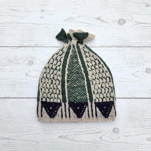 Può includere: Un berretto in maglia con un motivo geometrico in crema, verde bosco e blu navy scuro. Il cappello presenta un design a maglia testurizzata con pannelli verticali e una parte superiore arricciata, rifinito con triangoli blu navy sul bordo.