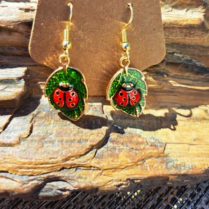 May include: Gold earrings with a green leaf design and a red ladybug on each leaf.
