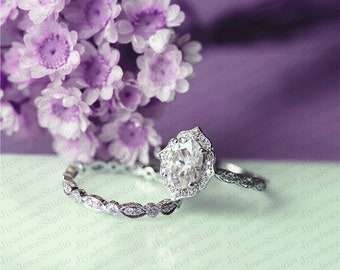 May include: A silver engagement ring set with a large oval-shaped center stone surrounded by smaller stones. The ring is set on a delicate band with a matching wedding band.