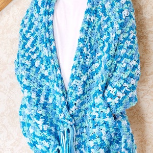 May include: A blue, green, and white crocheted cardigan with fringe on the bottom. The cardigan is open in the front and has a loose fit.