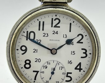 May include: A silver-toned pocket watch with a white dial featuring black Arabic numerals for 1 through 12 and smaller inner numerals for 13 through 24. The watch face displays the text REGINA and SWISS MADE, with a sub-dial for seconds.
