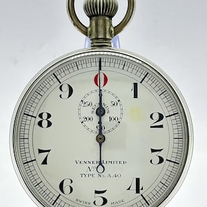 Op de afbeelding: Een zilverkleurige metalen stopwatch met een witte wijzerplaat, zwarte Arabische cijfers van 1 tot 9 en een sub-wijzerplaat met het label SECONDS en markeringen van 50 tot 250. De wijzerplaat bevat de tekst VENNER LIMITED, No, TYPE No. A.40 en SWISS MADE.