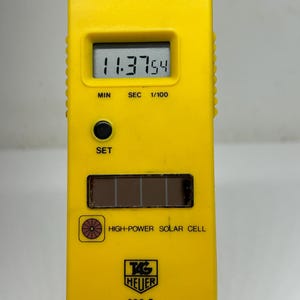 May include: A yellow TAG Heuer 200 S stopwatch with a digital display showing 11:37.54. It has buttons for SPL/RESET, START/STOP, and SET. Features include a solar cell and is designed for timing events.