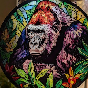 May include: A stained glass window hanging with a colorful depiction of a gorilla in a jungle setting. The gorilla is in the center of the image and is surrounded by green leaves and flowers.