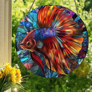 May include: A stained glass window hanging features a colorful betta fish with red, orange, blue, and purple scales. The fish is swimming with its fins spread out.