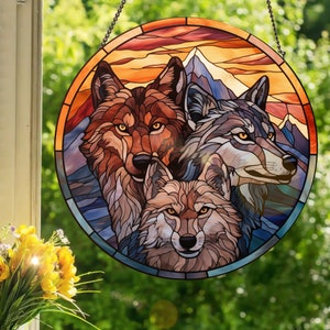 Puede incluir: Un panel de vitral con tres lobos sobre un fondo de montaña y puesta de sol. Los lobos son marrones, grises y tostados con ojos naranjas. El fondo es un naranja, amarillo y azul vibrante.