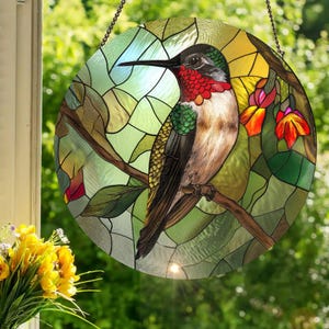 Puede incluir: Una ventana redonda de vidrieras con un colibrí posado en una rama. El ave tiene plumas rojas, verdes y marrones. El fondo es un mosaico de vidrio verde, amarillo y azul, con una cadena para colgar.