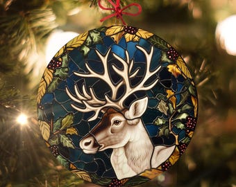 Könnte beinhalten: Ein runder Weihnachtsbaumschmuck aus Buntglas mit einer detaillierten Illustration eines Weißwedelhirsches mit Geweih vor einem blauen und grünen Hintergrund mit Stechpalme und Beeren.