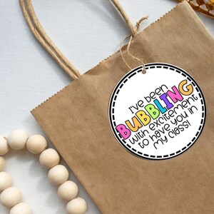 May include: A round gift tag with a white background and black border. The tag has the text "I've been BUBBLING with excitement to have you in my class!" in colorful letters.