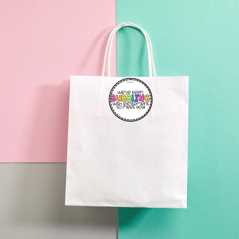 May include: White paper gift bag with a round sticker that says "We've been BUBBLING with excitement to meet you". The sticker has a black outline and colorful letters.