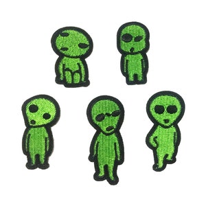 May include: Five green embroidered iron-on patches of cartoon aliens with black outlines. The aliens have different facial expressions and some have sunglasses.