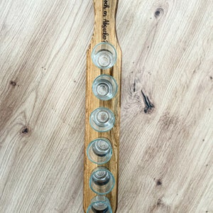 Pode incluir: Suporte de madeira para seis copos de shot. O suporte tem uma al&ccedil;a com o texto "Noch en Absacker?" gravado nele.
