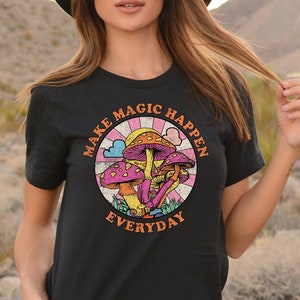 Puede incluir: Camiseta negra con un gráfico retro de setas y el texto "Make Magic Happen Everyday".