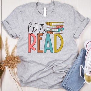 May include: Gray t-shirt with the text "Let's Read" in colorful letters and a stack of books with a leopard print design.