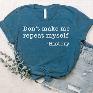 May include: Teal t-shirt with the text "Don't make me repeat myself. -History" in white. The shirt is knotted at the waist and paired with denim shorts. A sprig of greenery is placed near the shirt.