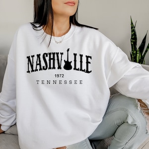 May include: White sweatshirt with black text that reads "NASHVILLE 1972 TENNESSEE" with a guitar graphic.