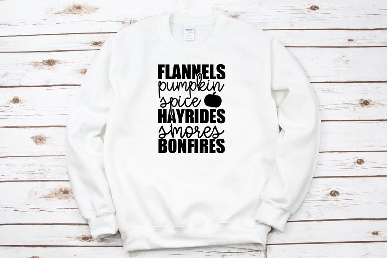 May include: White sweatshirt with black text that reads "Flannels pumpkin spice HAYRIDES smores BONFIRES" with a small pumpkin graphic.