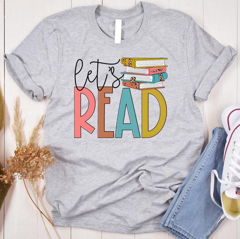 May include: Gray t-shirt with the text "Let's Read" in colorful letters and a stack of books with a leopard print design.