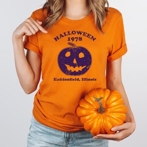 May include: Orange t-shirt with a purple pumpkin graphic and the text "Halloween 1978 Haddonfield, Illinois".
