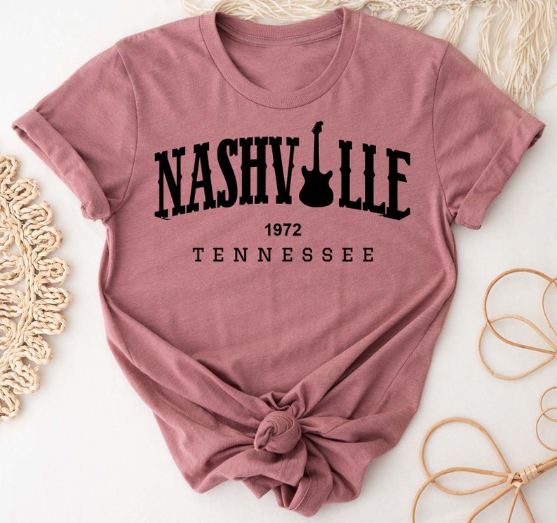 May include: A mauve colored t-shirt with a black graphic that says "NASHVILLE 1972 TENNESSEE" with a guitar silhouette.