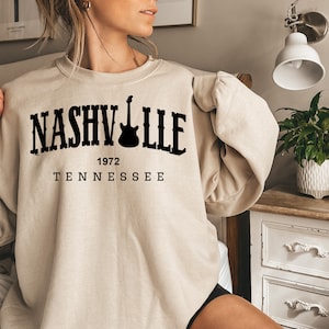 May include: A beige sweatshirt with black text that reads "NASHVILLE 1972 TENNESSEE" and a guitar graphic.