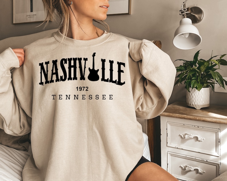 May include: A beige sweatshirt with black text that reads "NASHVILLE 1972 TENNESSEE" and a guitar graphic.