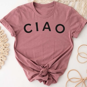 May include: A mauve colored t-shirt with the word "CIAO" printed in black on the front.