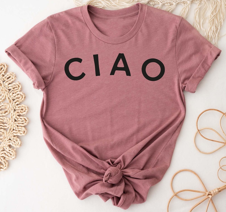 May include: A mauve colored t-shirt with the word "CIAO" printed in black on the front.