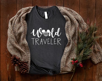 Puede incluir: Una camiseta gris oscuro con el texto "World Traveler" en letras blancas. El texto incluye un globo terráqueo blanco con dos orejas de ratón encima.