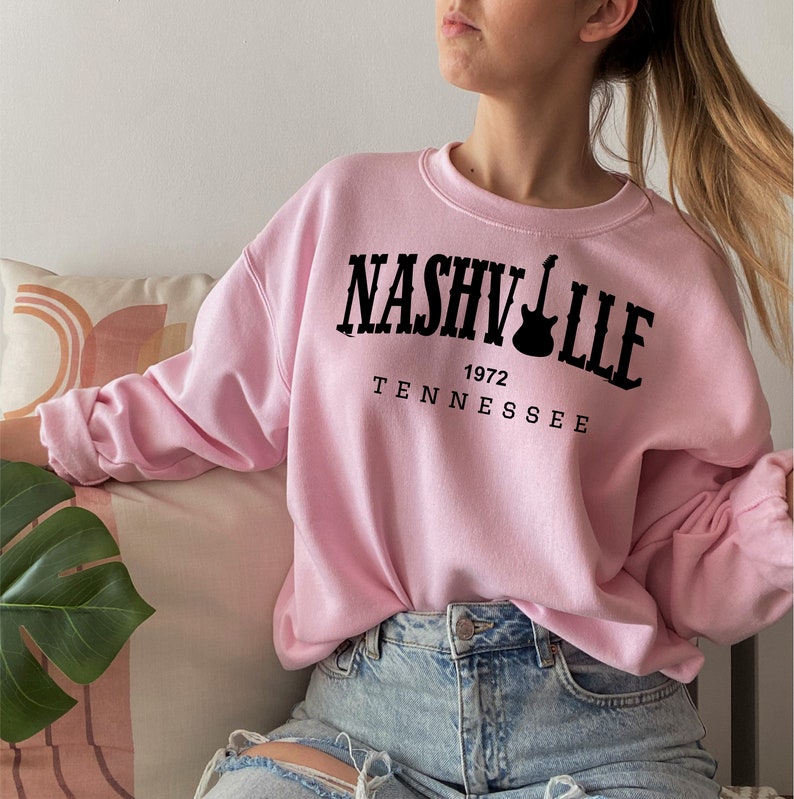 May include: Pink sweatshirt with black text that reads "Nashville 1972 Tennessee" and a guitar graphic.