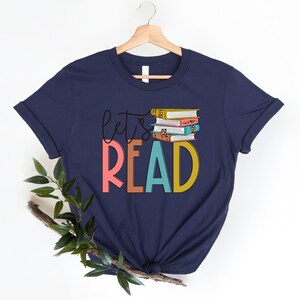May include: Navy blue t-shirt with the text "Let's Read" in colorful letters and a stack of colorful books on top of the word "Read".