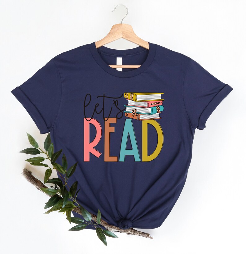 May include: Navy blue t-shirt with the text "Let's Read" in colorful letters and a stack of colorful books on top of the word "Read".